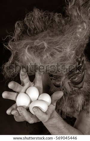 closeup portrait of an adult red-haired man-rooster with long hair and beard holding eggs in her hands 