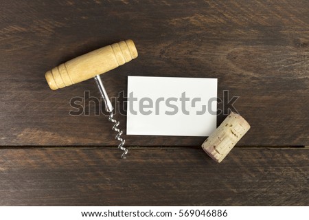 Photo of an old-fashioned corkscrew with a cork, shot from above on a dark brown background texture with a blank business card for copy space. Design template for a wine list or a tasting invitation