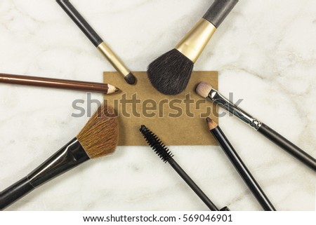 Makeup brushes and pencils on a light background, with a blank kraft business card for copy space. A horizontal template for a makeup artist's business card or flyer design