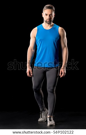Handsome athletic man in sportswear posing and looking at camera isolated on black 