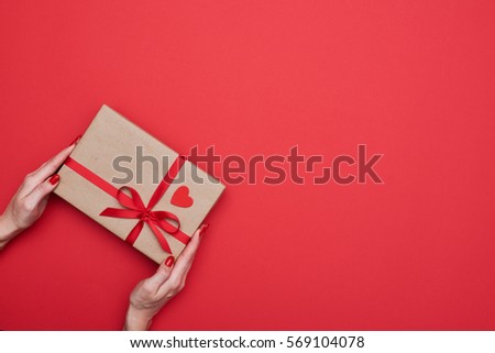 High angle of hands diagonally holding present box wrapped with red ribbon isolated over red flat lay background 