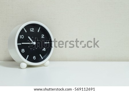 Closeup black and white alarm clock for decorate in a quarter to eleven or 10:45 a.m. on white wood desk and cream wallpaper textured background with copy space