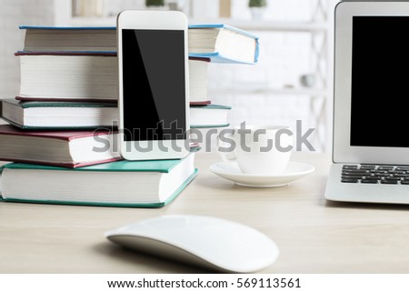 Blank mobile phone, laptop, coffee cup and books on light wooden desktop. Close up, Mock up
