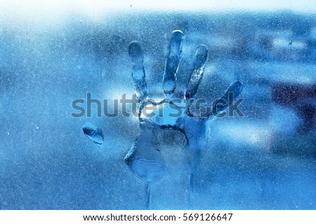 The imprint of the palm of human hand on frozen window glass in cool colors. Conceptual photography with an idea for reflection