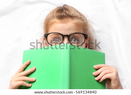 Cute girl with book lying on white sheets