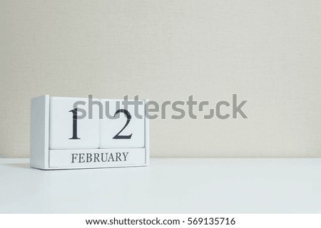 Closeup white wooden calendar with black 12 february word on blurred white wood desk and cream color wallpaper in room textured background with copy space in selective focus at the calendar