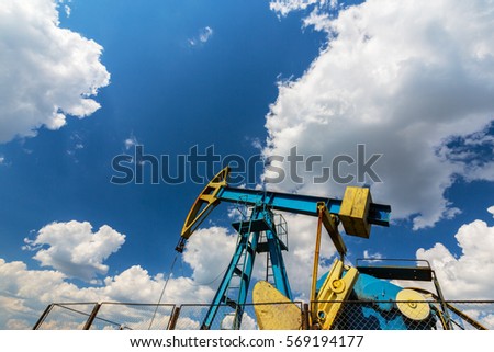 Operating oil and gas well in European oil field, profiled on blue sky with cumulus clouds, in spring