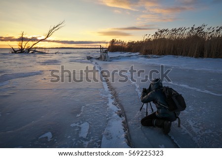 Photographer take pictures on the ice near the shore during sunset