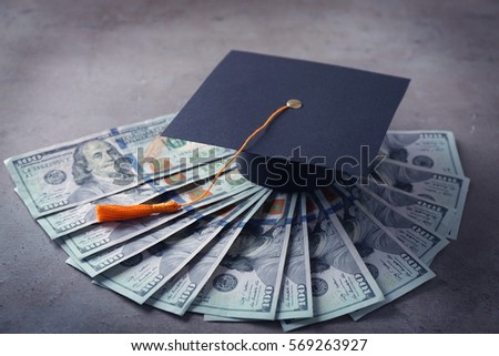 Graduation hat and dollar banknotes on table. Tuition fees concept Royalty-Free Stock Photo #569263927