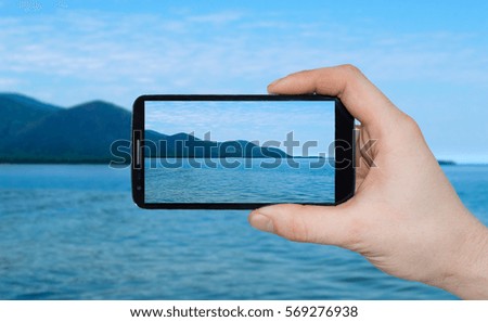 A man  hand holding smart phone making photo on smartphone mobile closeup sea mountain view