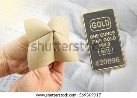 Hands in a paper fortune teller makes multiple decisions in front of a background of a gold bar in a seller's hand. Gold is a precious metal that every countries keep for their national reserve.