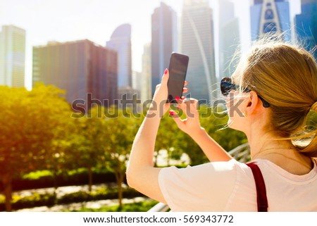 Wind blows woman's hair while she takes picture of beautiful skyscrapers on her iPhone