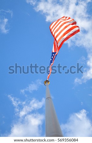 Flag of the United States of America in the summer sunny sky. USA flag hangs on the pole with wind, blue sky and clouds. Unfiltered, with natural lighting.