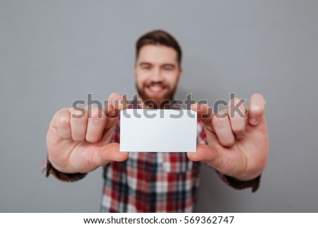 Image of attractive bearded man showing copyspace business card to camera. Focus on card.