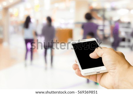 Man use mobile phone , blur image of shopper in the mall as background.