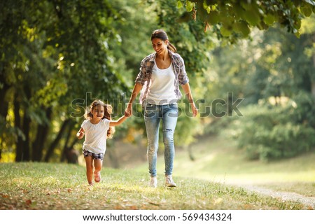 Mother and daughter playing and running around the park on beautiful morning. Royalty-Free Stock Photo #569434324
