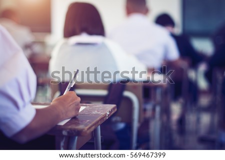 Student hand holding pen writing doing examination with blurred abstract background university students in uniform attending exam classroom educational school Royalty-Free Stock Photo #569467399