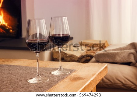closeup of two glasses with red wine on table in living room with fireplace in the background