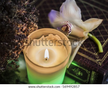 Green candle burning in the dark. White orchid on the background of album with photos