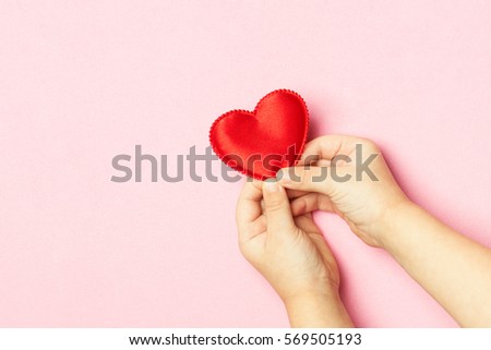 Children's hands holding the heart on a pink background. Concept of love, care, faith, hope, purity. Place for text. Flat fly