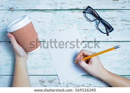 Female hands with a glass, paper, pencil on a white wooden background
