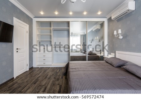 Contemporary bedroom design in a luxurious apartment. Hardwood floor, painted blue walls, white chandelier, rolling door wardrobe with mirrors. Royalty-Free Stock Photo #569572474