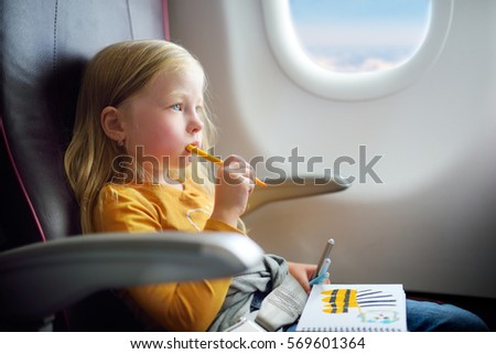 Adorable little girl traveling by an airplane. Child sitting by aircraft window and drawing a picture with colorful felt-tip pens.  