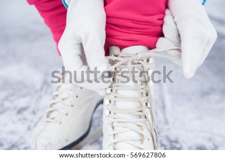 Woman tying white skates on the ice area in winter day. Weekends activities outdoor in cold weather.