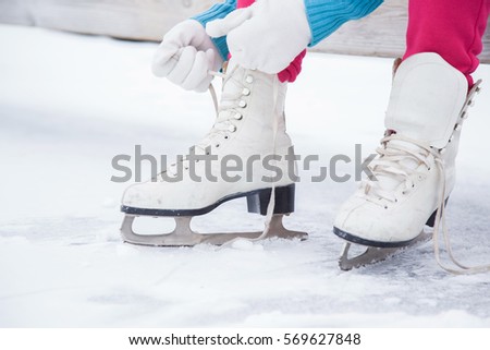 Woman tying white skates on the ice area in winter day. Weekends activities outdoor in cold weather.