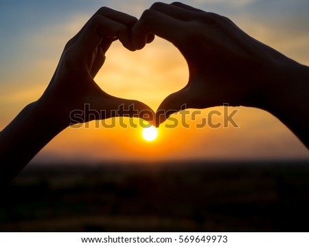 Woman making heart of hands at sunset