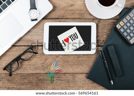 I Love You written on tablet computer, office desk with electronic devices, computer and paper, wood table from above, concept image for blog title or header image.