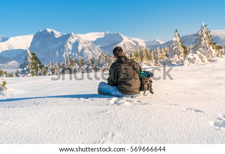 young man sitting on the snow with a beautiful snowy mountain landscape on the background