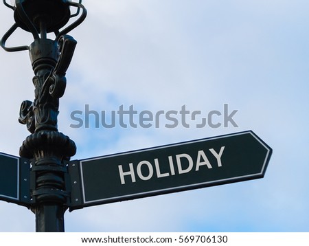 Street lighting pole with conceptual message HOLIDAY on directional arrow over blue cloudy background.