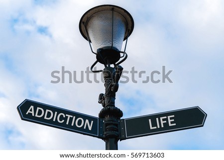 Street lighting pole with two opposite directional arrows over blue cloudy background. Addiction versus Life concept.