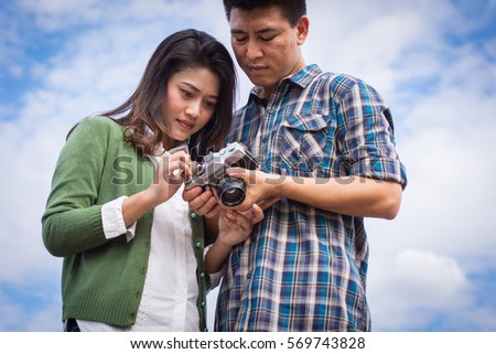 Young men and young women Couple together standing on bench waterfront port in the park. Handle vintage camera.