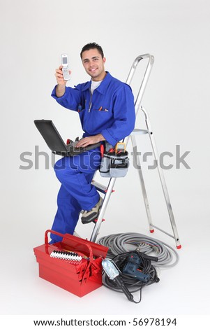 Electrician in overalls with a mobile phone and a laptop computer on white background