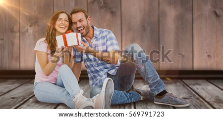 Happy young couple holding gift against graphic image of wooden planks