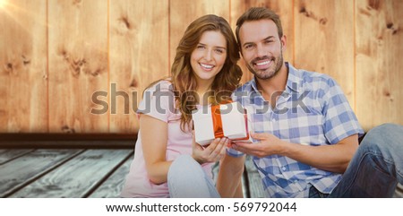 Happy young couple holding gift against image of wooden floor and wall