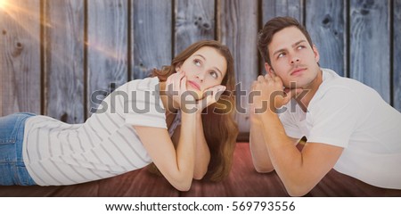 Couple lying on floor and looking up against brown wooden shelf on gray wall