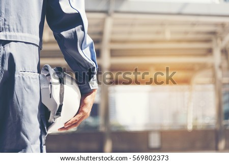 Construction safety engineer holding hard hat for safe work. Safety Suit Trust Team Holding White Yellow Safety hard hat Security Equipment on Construction Site. Hardhat Protect Civil Construction Royalty-Free Stock Photo #569802373