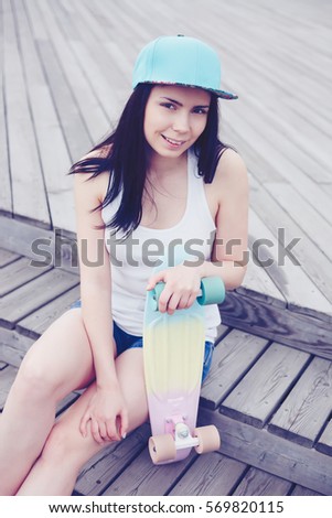 Happy young skater girl hold short cruiser skateboard deck in hands.Pretty brunette girl with friendly smile chilling outdoor with her skate board.Skateboarding in fun and healthy new urban transport