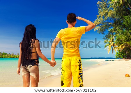 A loving couple, man and woman enjoying summer vacation on a tropical paradise beach with clear sea ocean water and scenic island on the horizon overgrown green palm on background blue summer sky