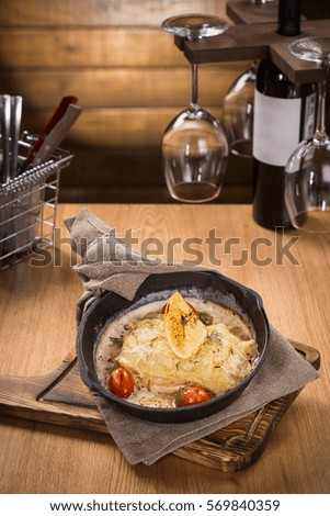 Halibut baked with cheese on black metal pan on wooden background.