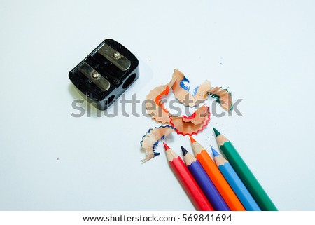 some colored pencils of different colors and a pencil sharpener and pencil shavings on a white paper