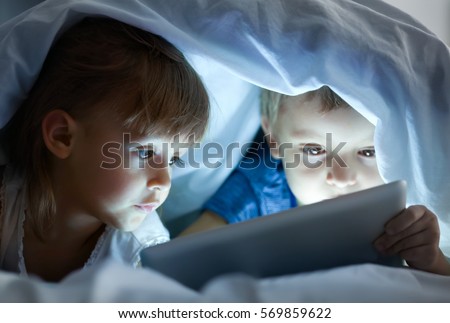 Cute little children lying under blanket with tablet computer Royalty-Free Stock Photo #569859622