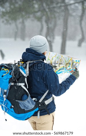 Tourist with backpack, map and navigation in the winter forest