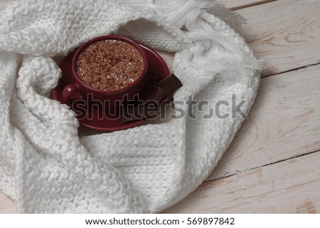 Milk chocolate in a cup on a saucer against a background of a scarf and a wooden background.