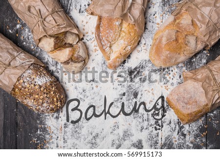 Baking and cooking concept background. Lots of different bread sorts, wrapped in craft paper top view with text on copy space in middle on wooden table, sprinkled with flour. Soft toning