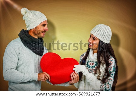 Smiling couple holding paper heart against yellow vignette