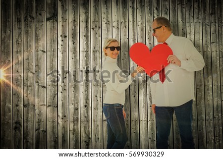 Older affectionate couple holding red heart shape against digitally generated grey wooden planks